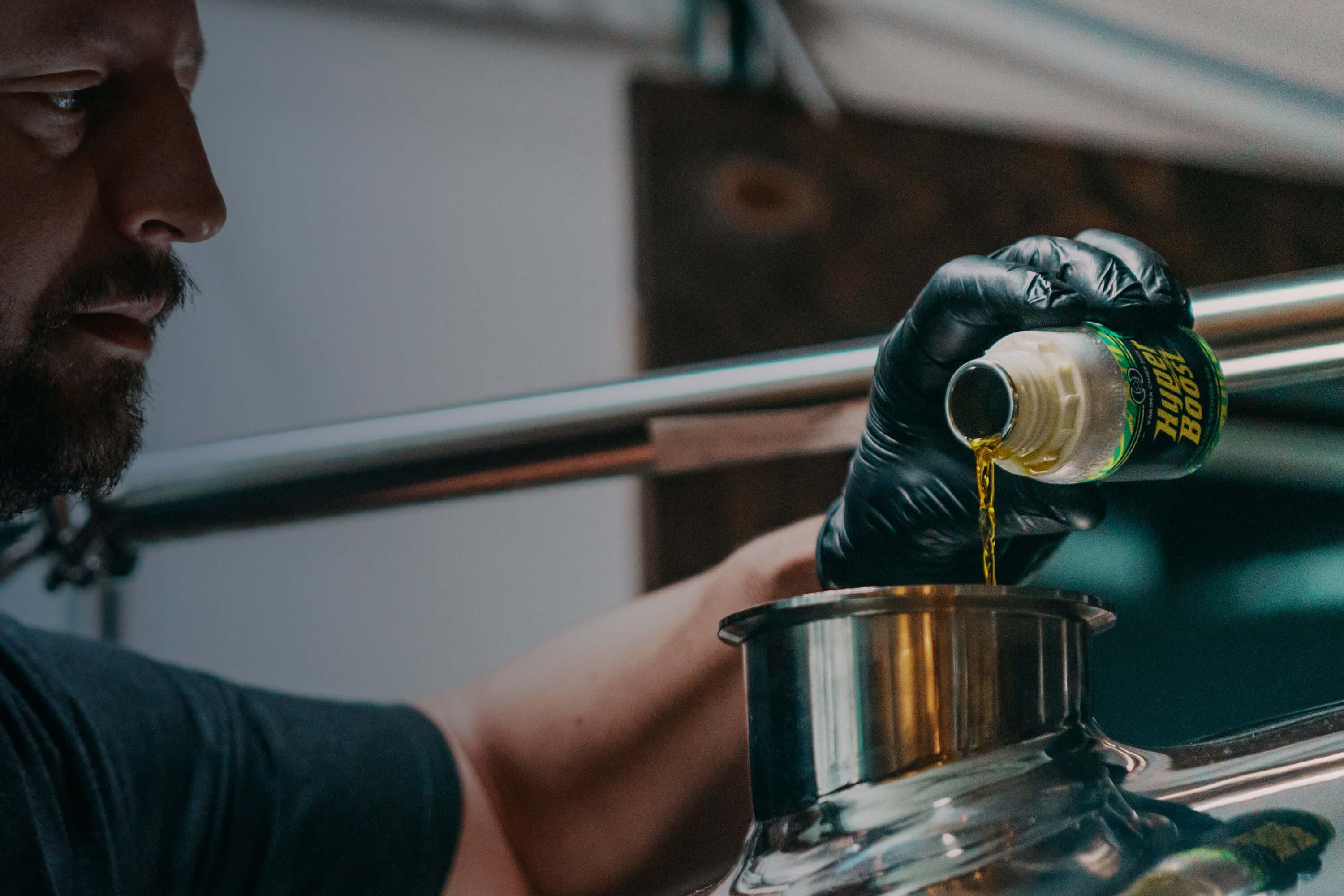 Brewer pouring a small HyperBoost bottle of flowable extract oil into tank